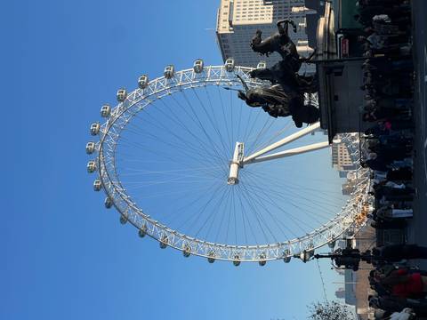       The London Eye towering against a bright blue sky.
  
