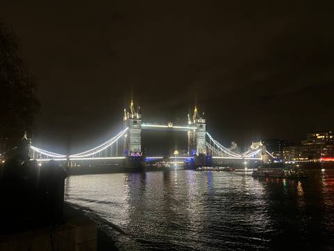 Tower Bridge lit up at night reflecting on the River Thames.