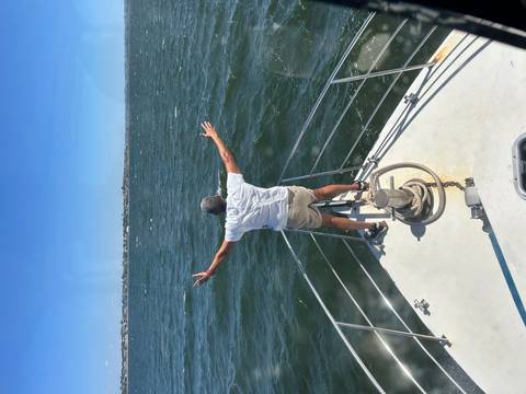 Person standing on a boat with arms outstretched facing the ocean.