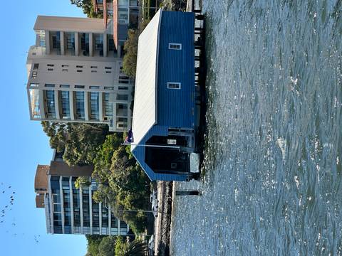 Blue boathouse on the water's edge with modern buildings in the background.