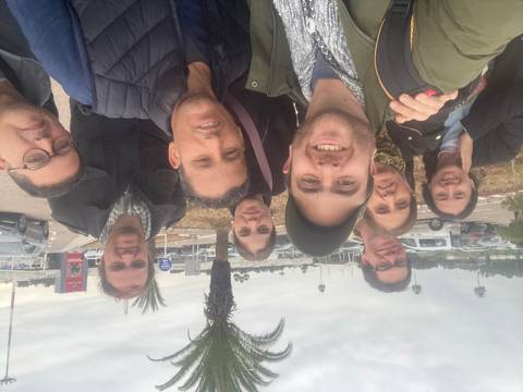 Group selfie with people outdoors near palm trees.