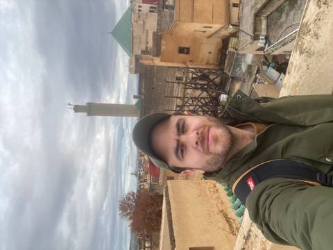 Person taking a selfie with cityscape and minaret in the background.