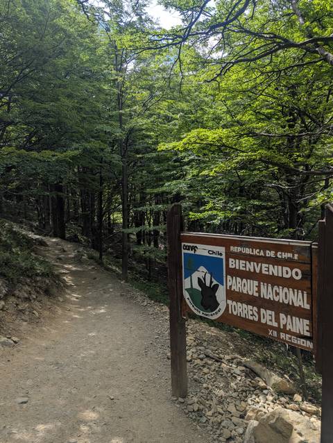 Entrance sign for Torres del Paine National Park beside a dirt trail.