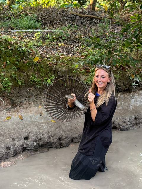 Woman holding a fish and smiling in a natural setting.