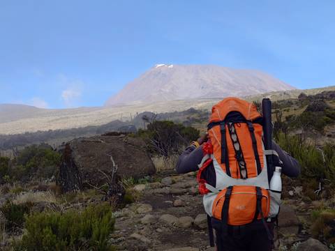       Hiker with backpack on a trail with mountains in the background.
  