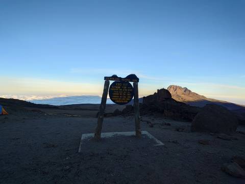 Kibo Hut sign with a mountain view behind.