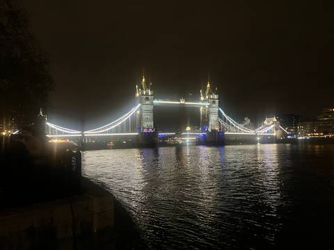 Tower Bridge illuminated at night, reflecting in the River Thames.