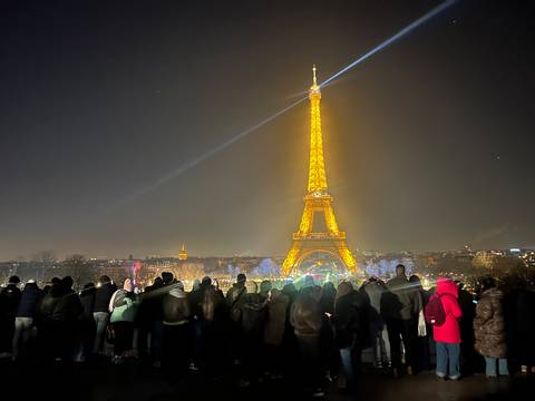       Eiffel Tower brilliantly lit at night with a crowd of people gathered.
  