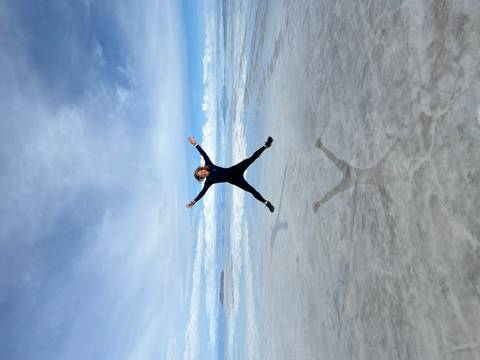 A woman jumping in the air on salt flats with her reflection.