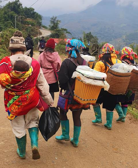 Group of people walking on a dirt path, carrying colorful baskets.