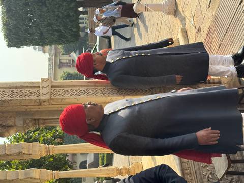 Two men wearing traditional attire with red turbans.