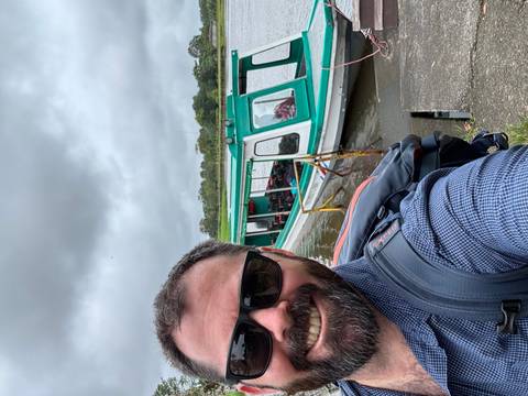       Selfie of a person with sunglasses near a boat on a river.
  