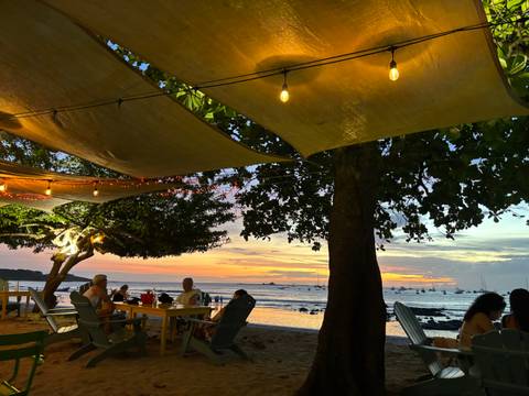 People dining outdoors under string lights with sunset view.