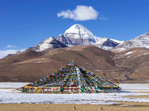 Mount Kailash covered in snow with colorful prayer flags in the foreground.