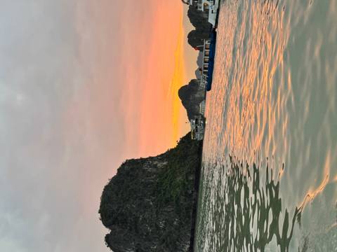 Sunset view over Halong Bay with boats and limestone cliffs.