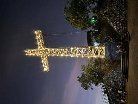 Illuminated cross structure at night with people gathered around.