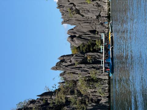 Tour boat on blue water with rocky cliffs in the background.