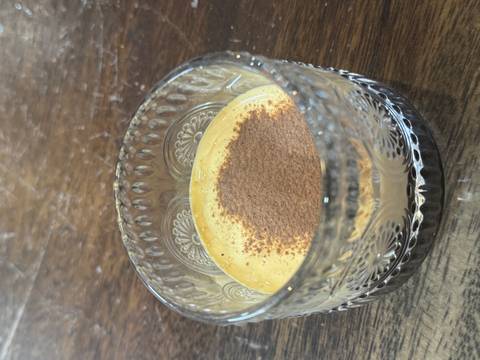Glass cup filled with a creamy dessert topped with cocoa powder.