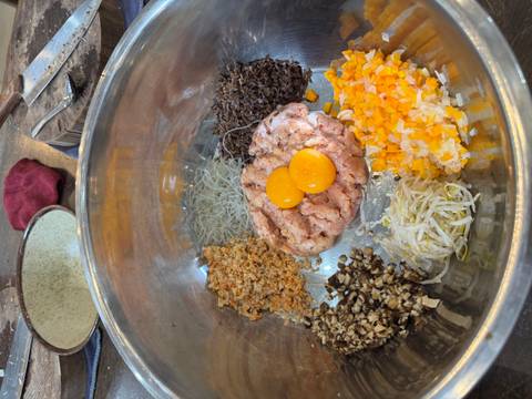 Bowl containing ingredients for a dish including meat, vegetables, and eggs.
