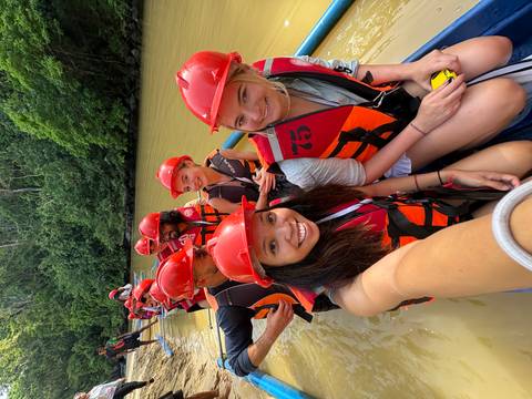 Group of people wearing red helmets and life jackets on a raft surrounded by lush vegetation.