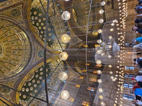 Interior of a historic mosque with an ornate ceiling and numerous visitors.
