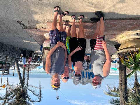 Group of travelers posing on a beach with resort and ocean in the background.