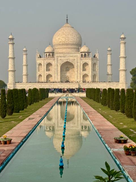      The Taj Mahal with people in front and its reflection in the water.
  