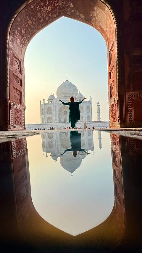       A person standing in front of the Taj Mahal with arms raised.
  