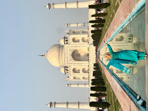 A person with open arms facing the Taj Mahal with reflection on the water.