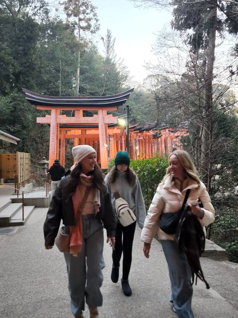 Three young women walking near traditional Japanese torii gates.