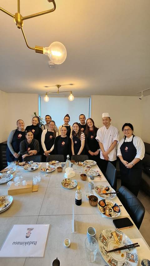      A group of people posing in a room with a chef during a cooking class.
  