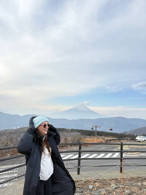 View of Mount Fuji under a cloudy sky with a person in the foreground.