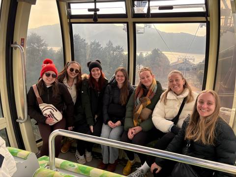       Group of friends in a cable car with a scenic mountain background.
  