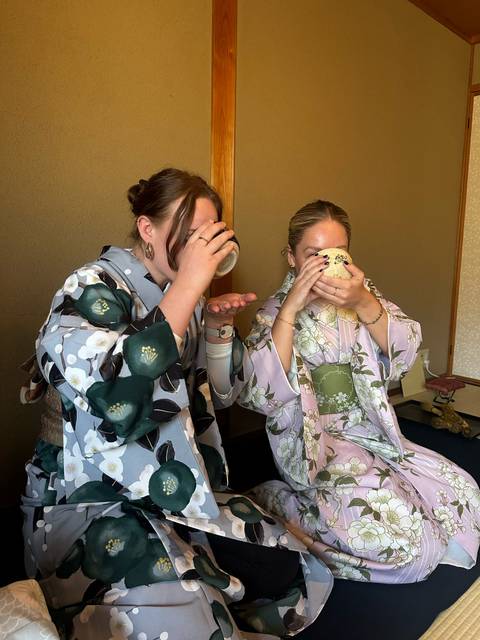       Two people in traditional clothing enjoying tea inside.
  
