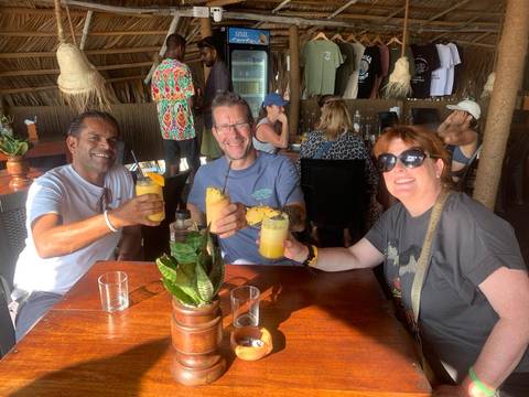 Three people sitting at a wooden table, each holding a tropical drink with pineapple garnishes, in an indoor setting.