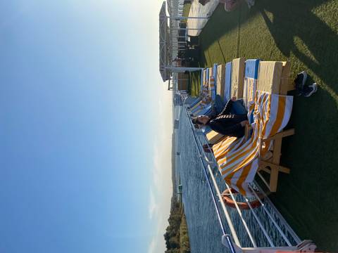 A person relaxing on a deck chair on a ship with a river view.
