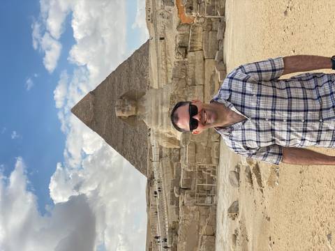 A person smiling in front of the Great Pyramid and Sphinx at Giza.