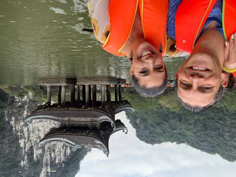 A couple wearing life jackets in a boat with a pagoda and limestone cliff in the background.