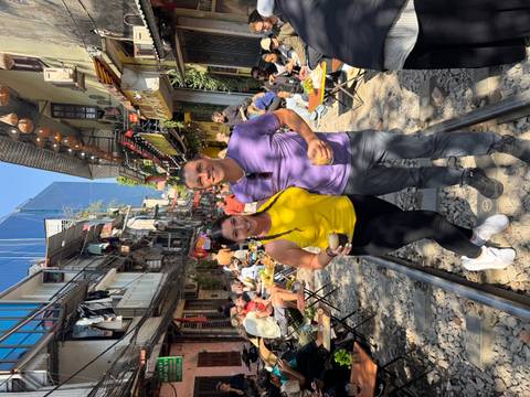 A couple standing on railway tracks in a crowded street with people dining outside.