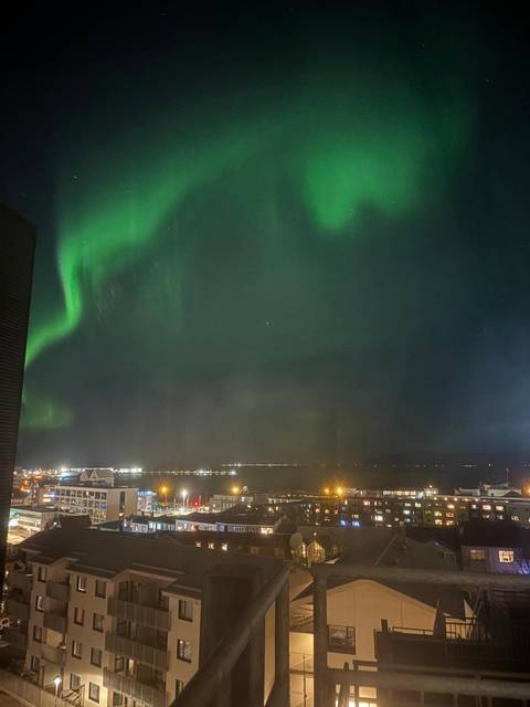 View of city lights under a vibrant green aurora borealis.