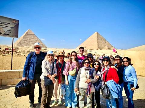 Large tour group posing in front of pyramids with a bright blue sky.