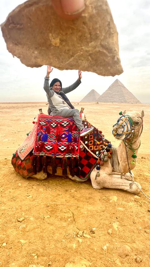 Person on a camel posing with pyramids in the desert.