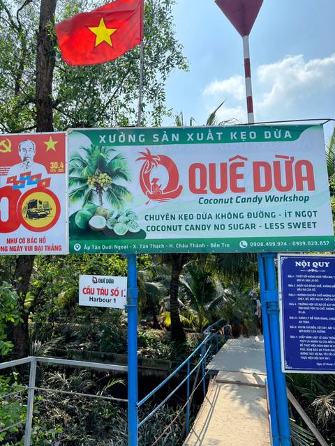       Quê Dừa Coconut Candy Workshop signboard surrounded by palm trees.
  