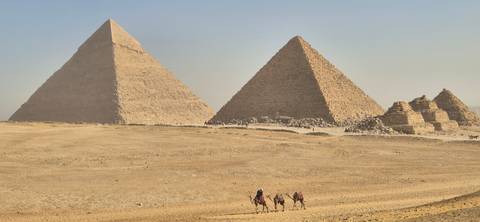       The pyramids of Giza with camels and people traversing the desert.
  