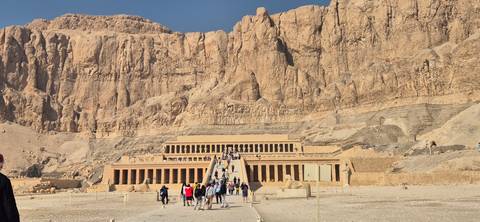       Tourists exploring an ancient temple carved into a cliff in the desert.
  