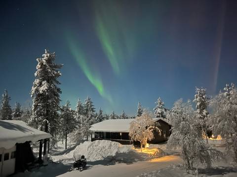 Northern lights over a snowy landscape with cabins in the foreground.