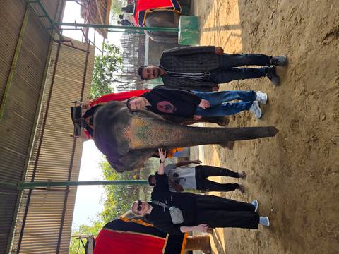 Tourists standing next to an elephant in what appears to be a rural setting.