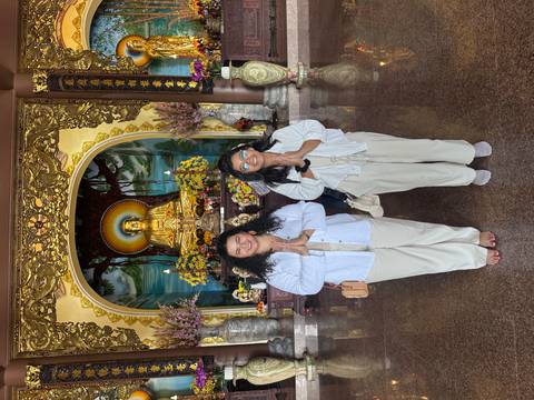       Two women posing and praying in front of a Buddha statue in an ornate temple.
  
