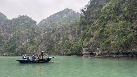       People on a small boat exploring caves in a lush, mountainous area.
  