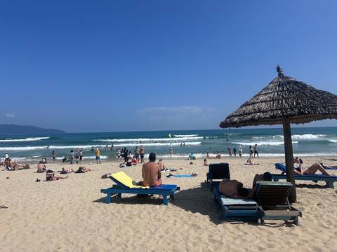       Beach scene with people sunbathing and playing in the ocean under a blue sky.
  